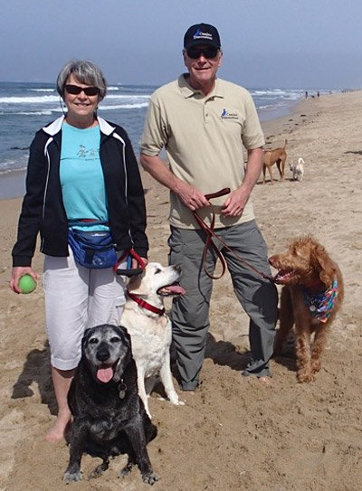 Shari Chris Sandburg holding dogs on a leash standing at the beach.